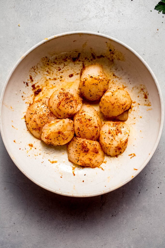 Seasoned scallops in white bowl before cooking.