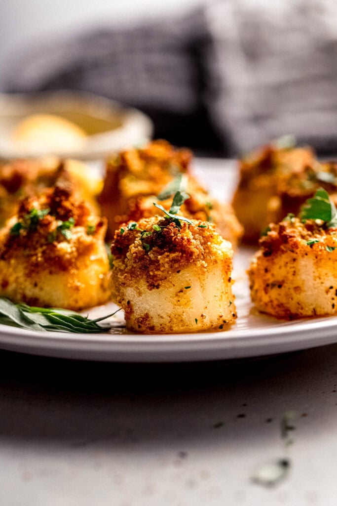 Side view of air fryer scallops on plate with lemon wedges.