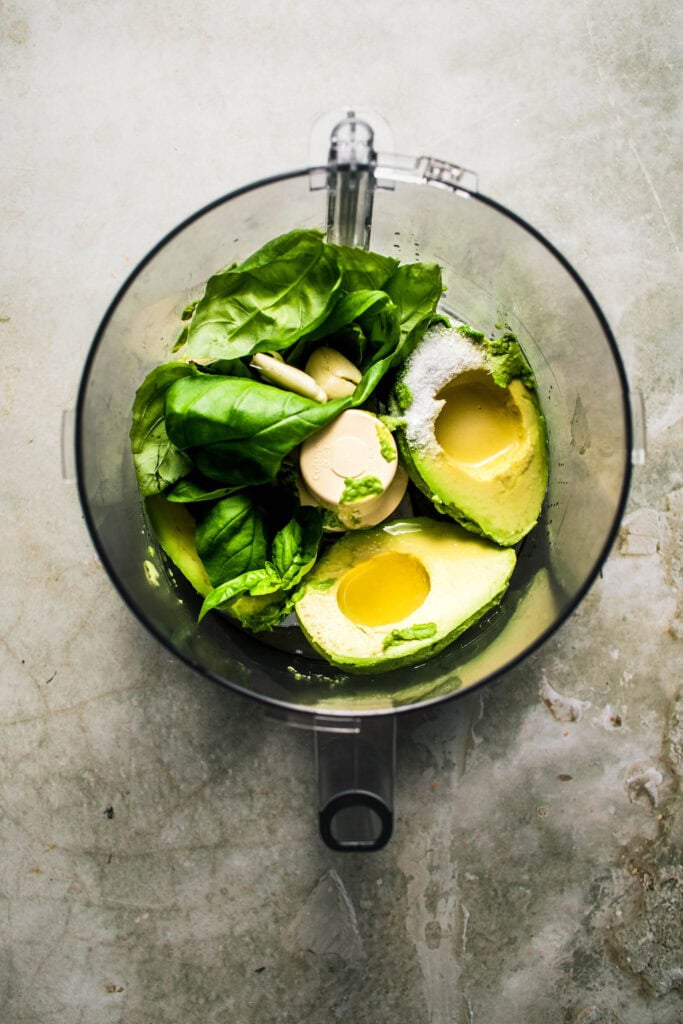 Avocados and basil in food processor bowl.