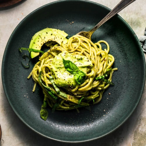 Pasta noodles tossed with creamy avocado pasta sauce served on greeen plate.