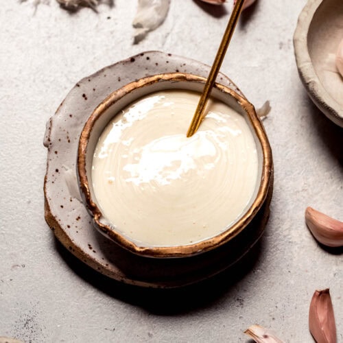 Finished garlic aioli in small bowl with gold spoon.
