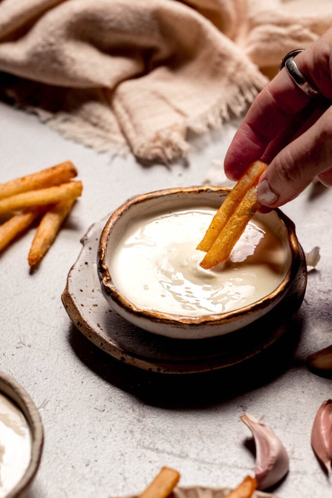 Fries dipping into bowl of garlic aioli.