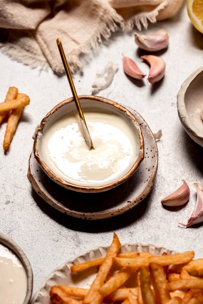Cheater garlic aioli in bowl next to plate of french fries.