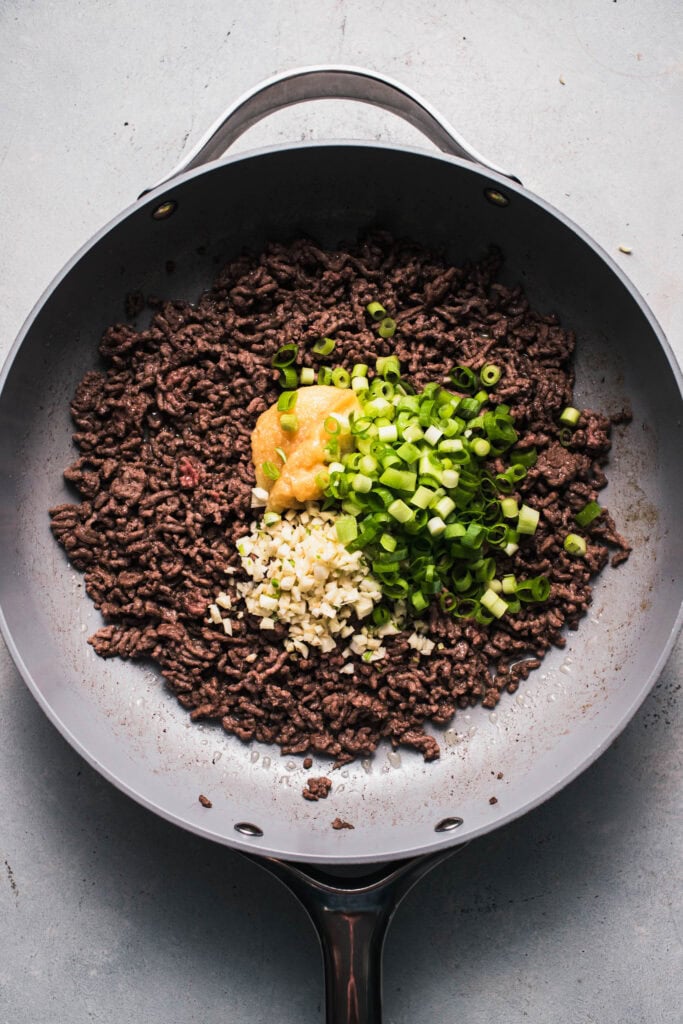 Ground beef in skillet with ginger, green onions and garlic.