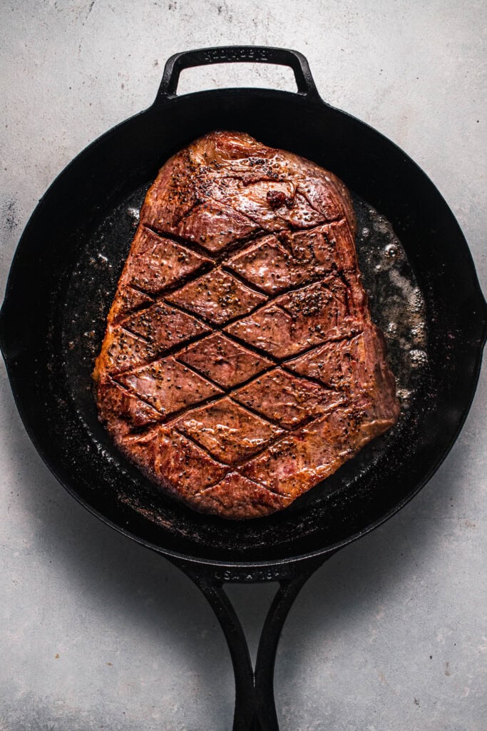 Flank steak being seared in skillet.