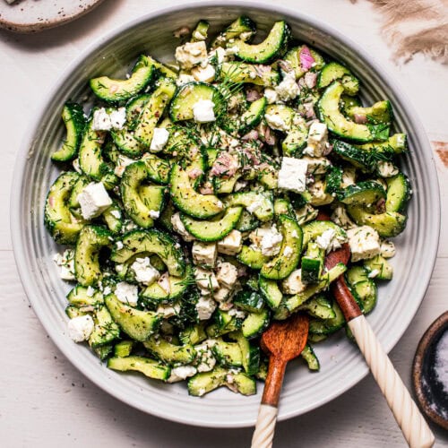 Overhead shot of feta cucumber salad in bowl with wooden serving spoons.