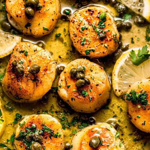 Overhead close up of scallop piccata topped with capers and served alongside lemon slices.