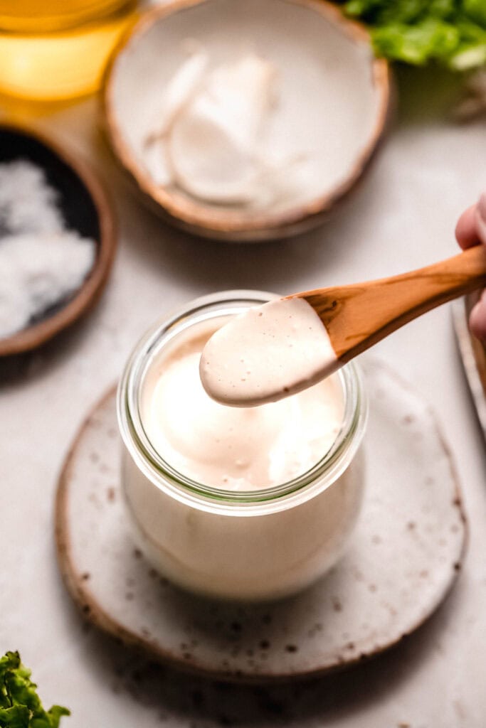 Hand dipping wooden spoon into small jar of tahini dressing.
