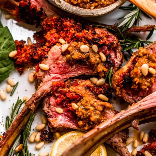 Lamb chops arranged on a serving platter, topped with sun-dried tomato pesto and served with a small bowl of pesto.