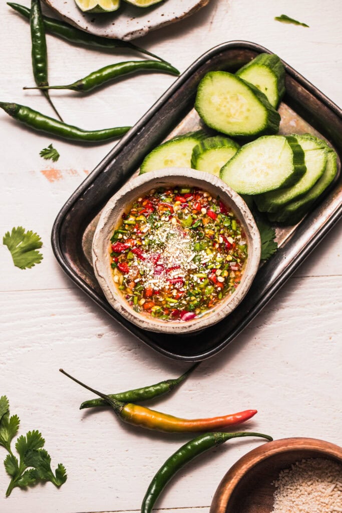 Finished crying tiger sauce in bowl next to sliced cucumbers.