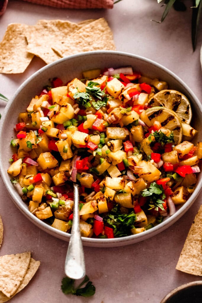 Side view of finished grilled pineapple salsa in serving bowl next to chips.