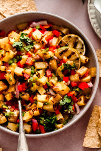 Side view of finished grilled pineapple salsa in bowl with serving spoon.