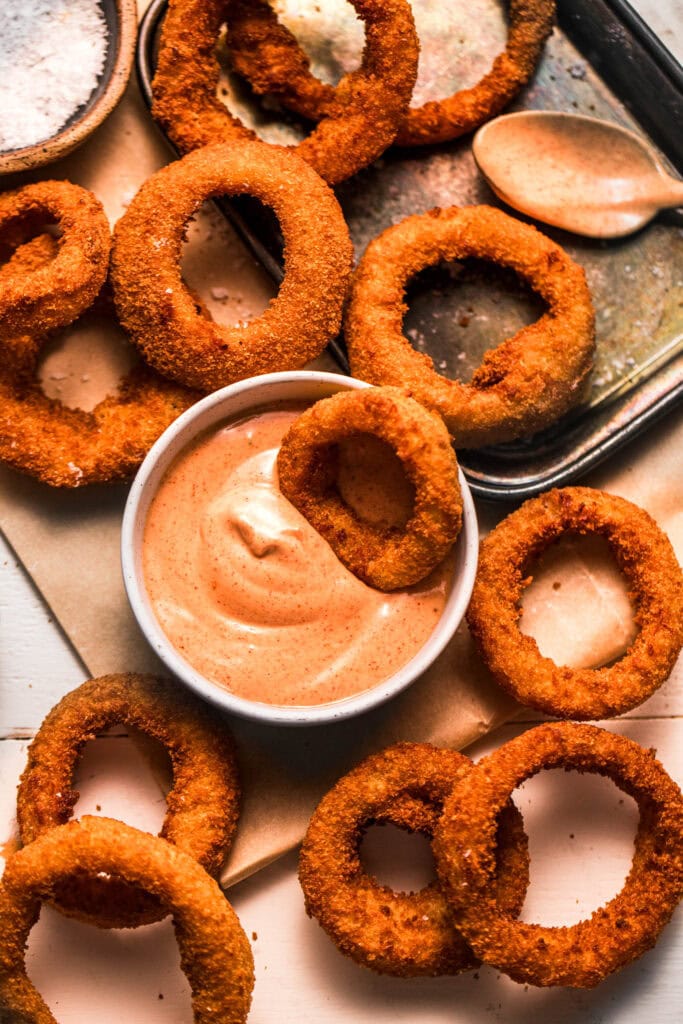 Crispy onion ring dipped into bowl of sauce.