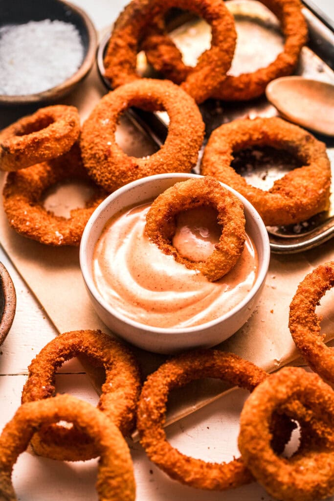 Side view of onion ring dipped into bowl of sauce.