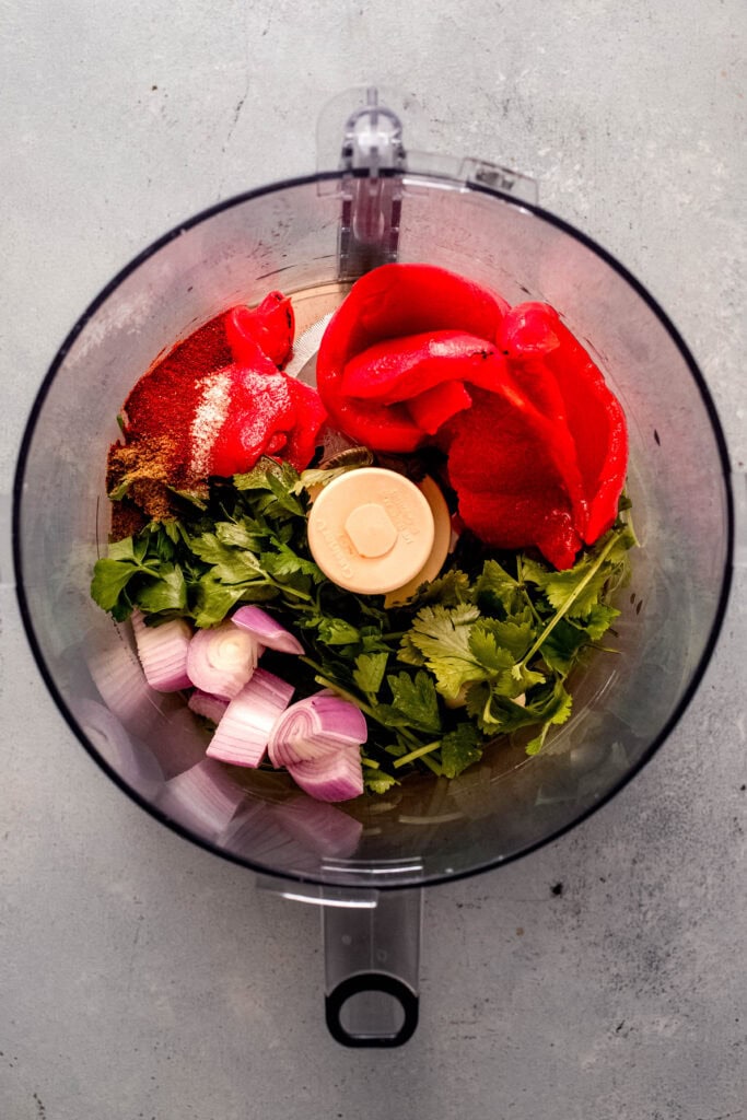 Red chimichurri sauce ingredients in food processor bowl before processing.