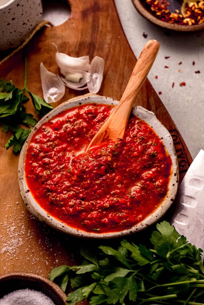 Red chimichurri sauce in small serving bowl with wooden spoon.