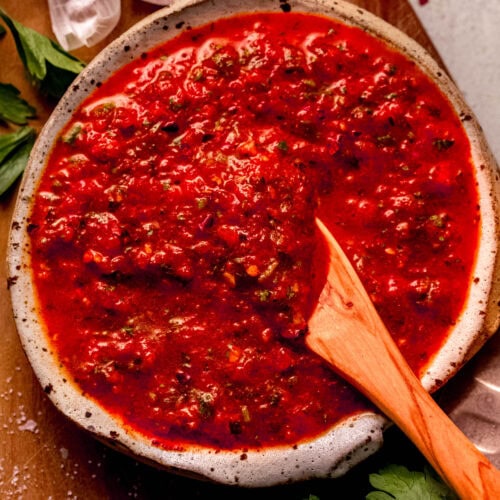 Close-up of red chimichurri in a serving bowl paired with a wooden spoon.