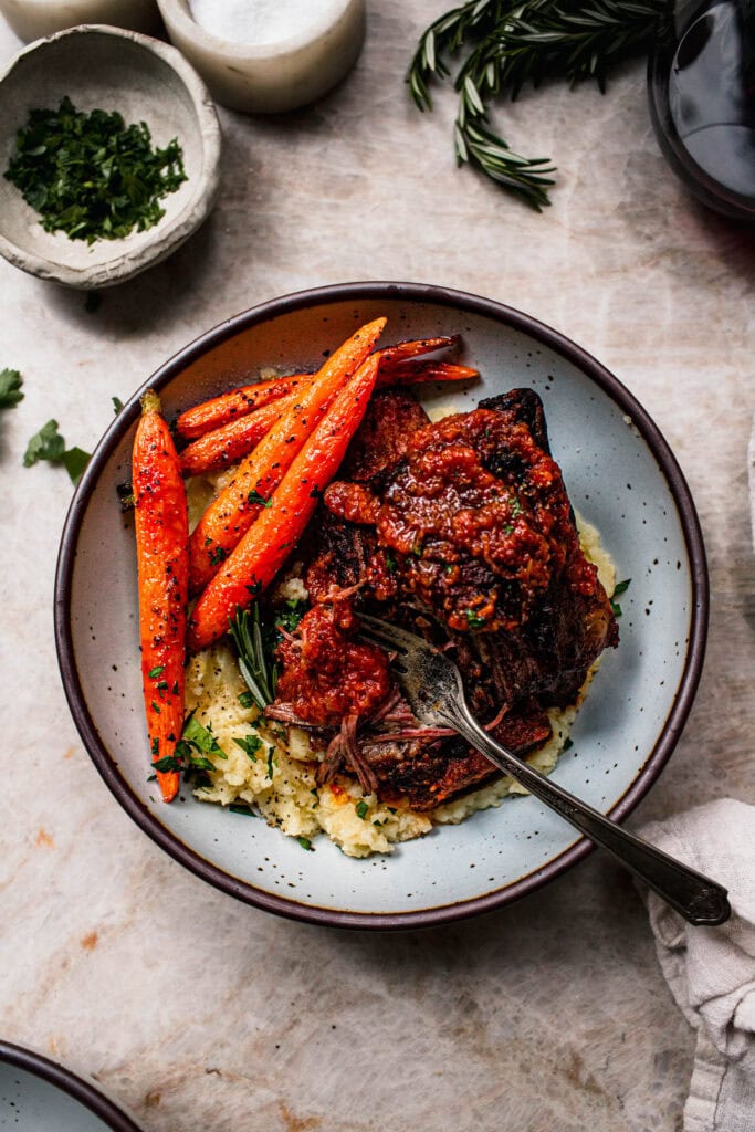 Finished tender short ribs served in bowl with mashed potatoes and roasted carrots.