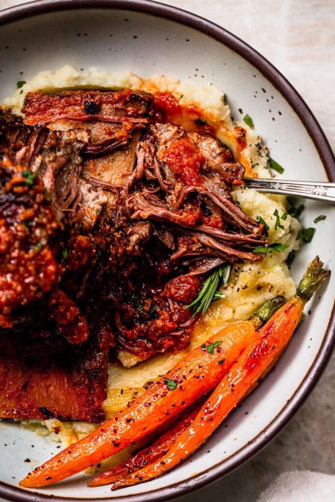 Shredded short ribs in bowl with carrots and mashed potatoes.