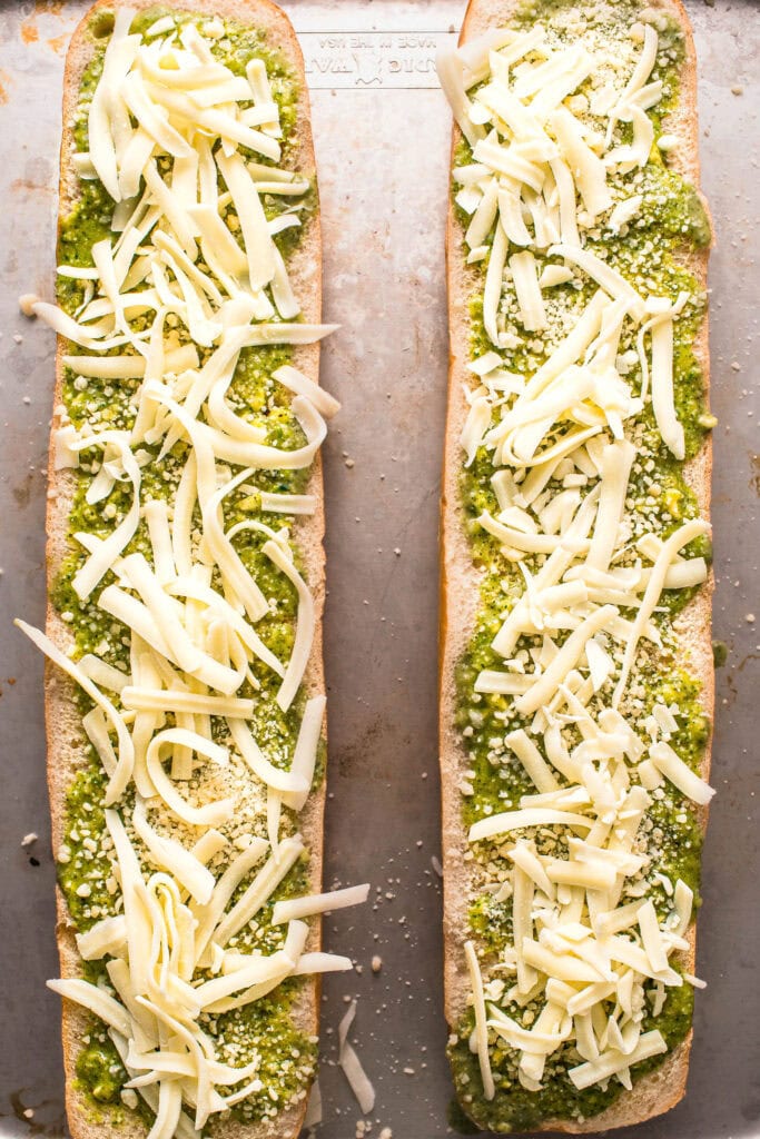Pesto garlic bread topped with cheese before baking.