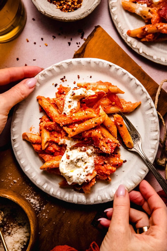 Hands holding plate of vodka rigatoni pasta.