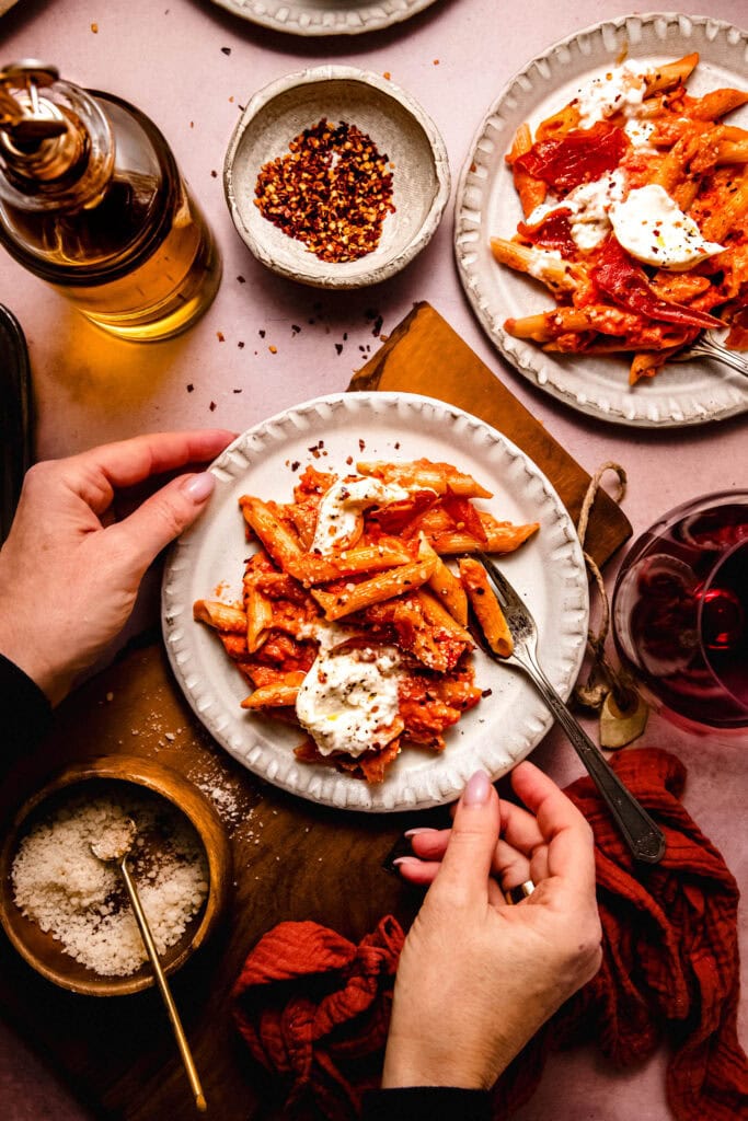 Hands holding plate of rigatoni with spicy vodka sauce.