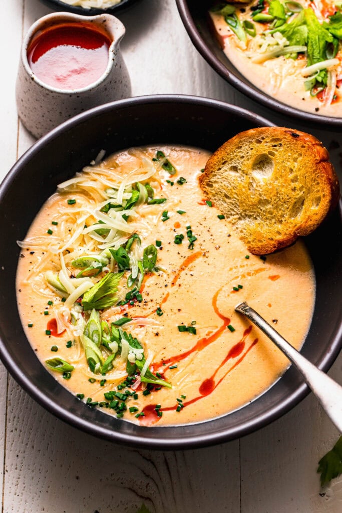 Overhead close up shot of buffalo cauliflower soup with bread dipping into it.
