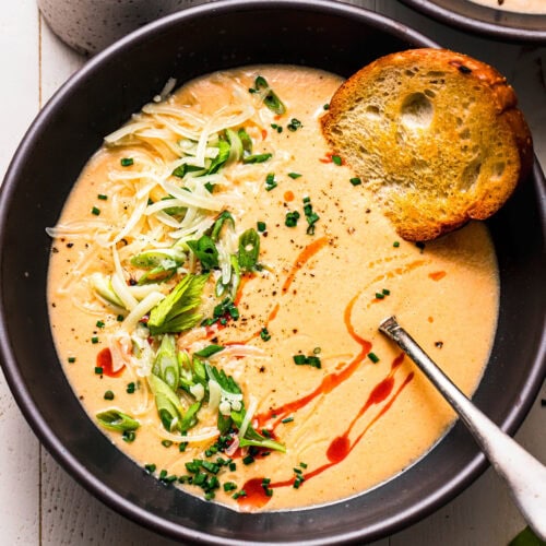 Buffalo cauliflower soup served in black soup bowl next to small jar of hot sauce.