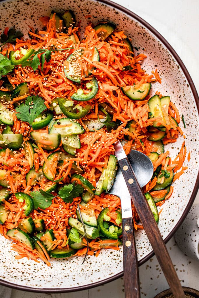Close up of carrot cucumber salad in bowl with tongs.