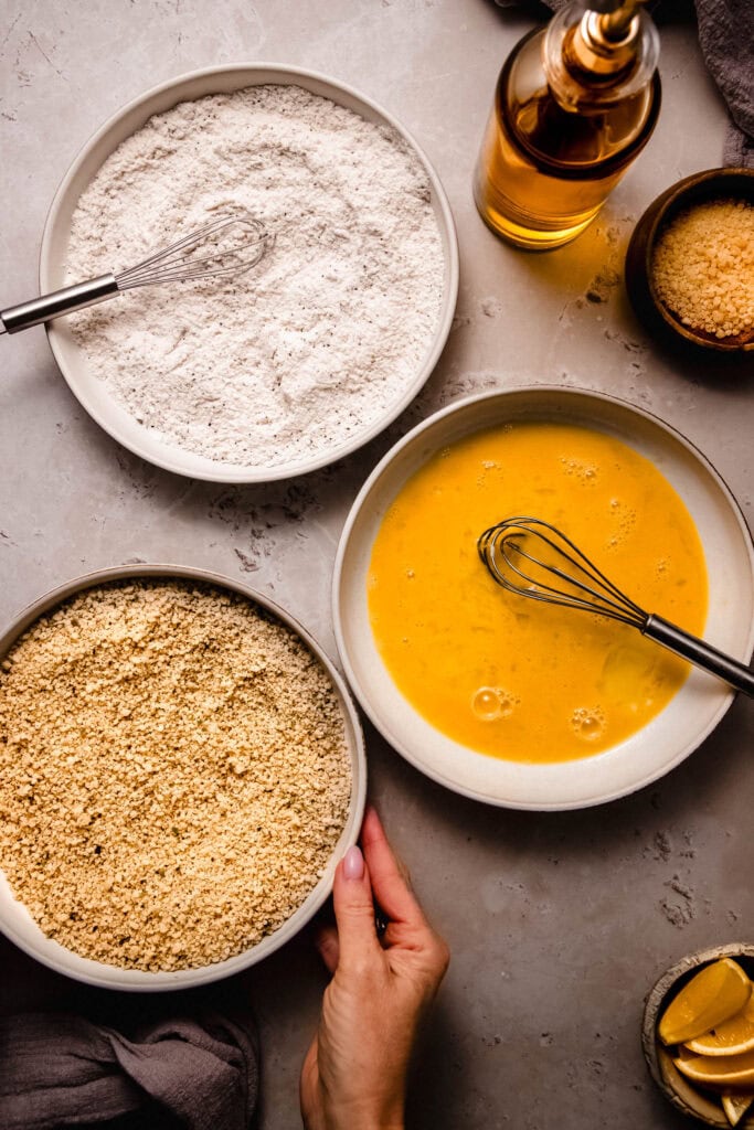 Bowls with eggs, flour and breadcrumbs on counter.