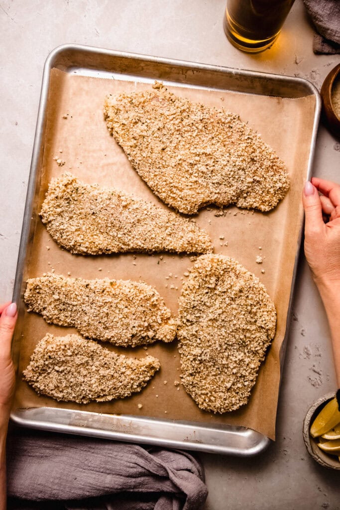 Breaded chicken breasts on baking sheet.