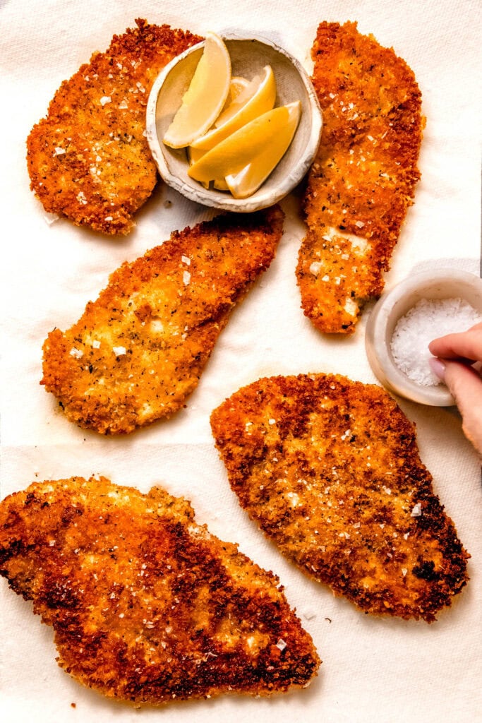 Hand sprinkling salt on chicken cutlets.