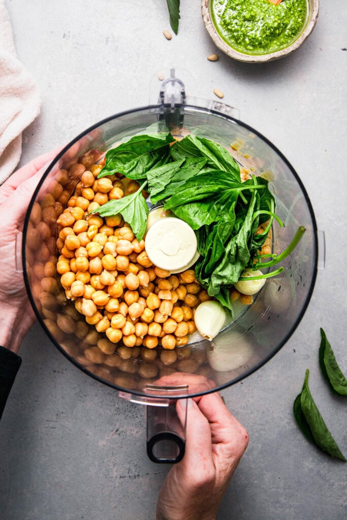 Ingredients for pesto hummus in food processor bowl before blending.
