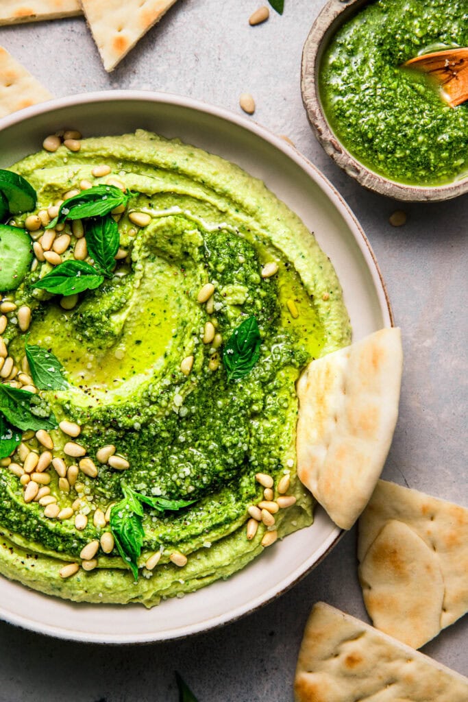 Pita bread dipping into bowl of hummus with pesto.
