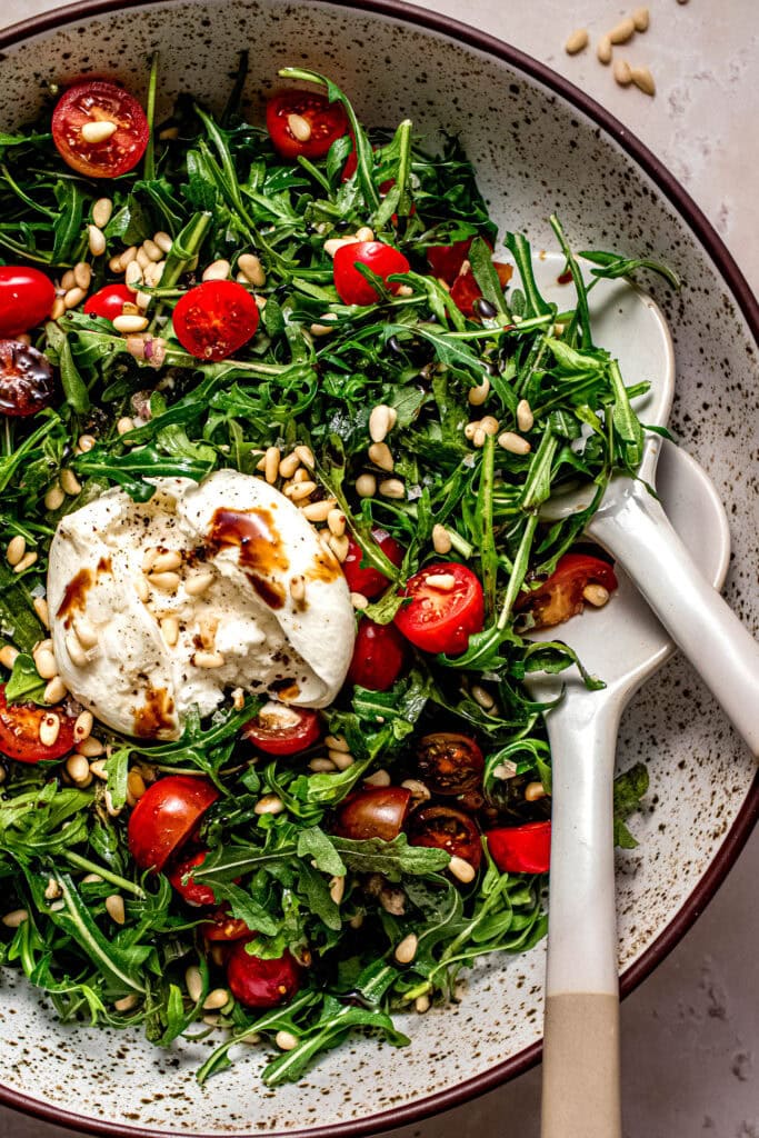 Overhead close up of arugula burrata salad in serving bowl.