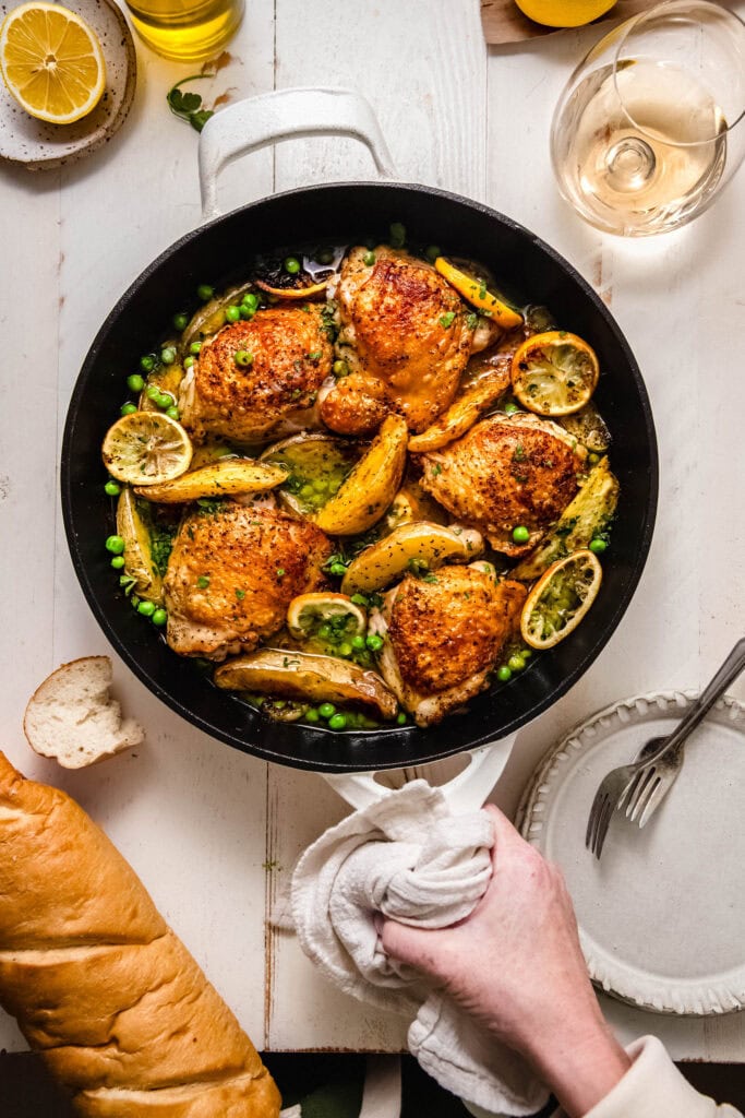 Hand holding skillet of chicken vesuvio.