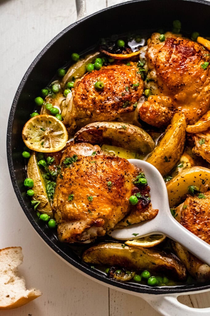 Side view of chicken vesuvio in skillet with serving spoon.