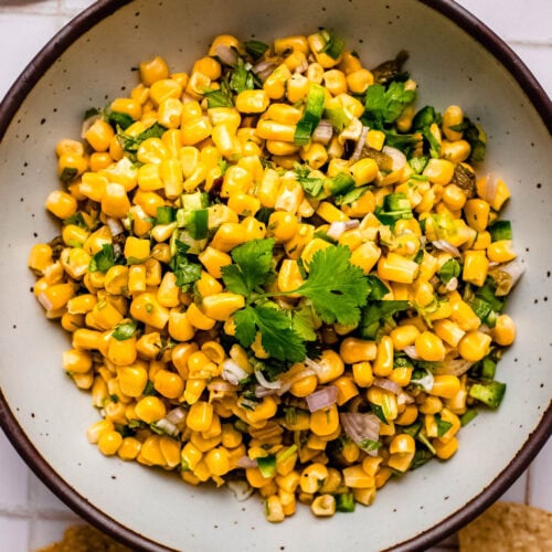 Copycat chipotle corn salsa in bowl on counter next to corn chips.