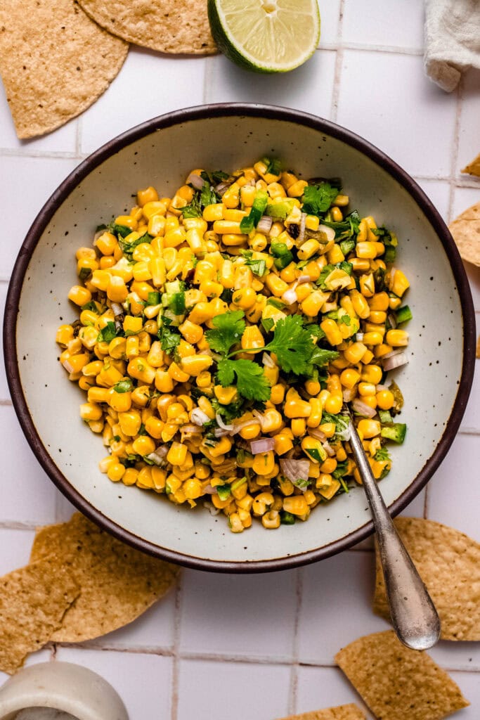 Copycat chipotle corn salsa in bowl on counter next to corn chips.