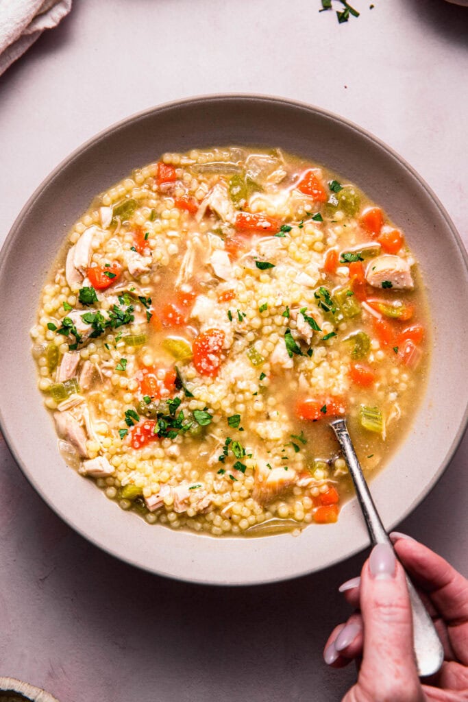Hand holding spoon dipping into bowl of pastina soup.