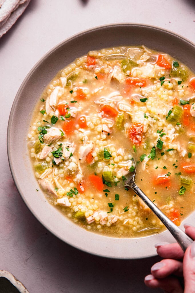 Close up of spoon dipping into pastina soup.