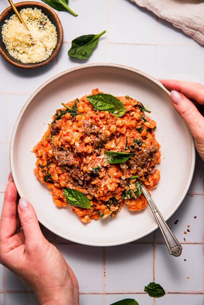 Hands holding bowl of pastina alla vodka with fork.