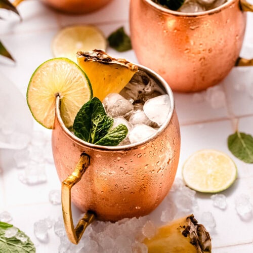 Side view of two pineapple moscow mule cocktails on counter.