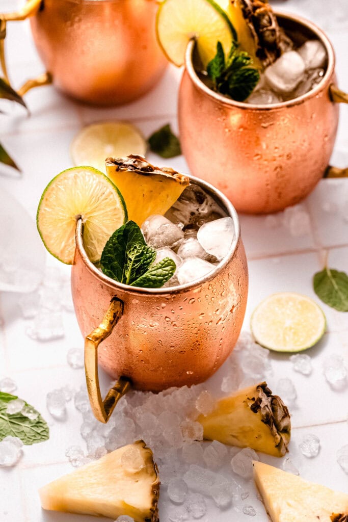 Side view of two pineapple moscow mule cocktails on counter.