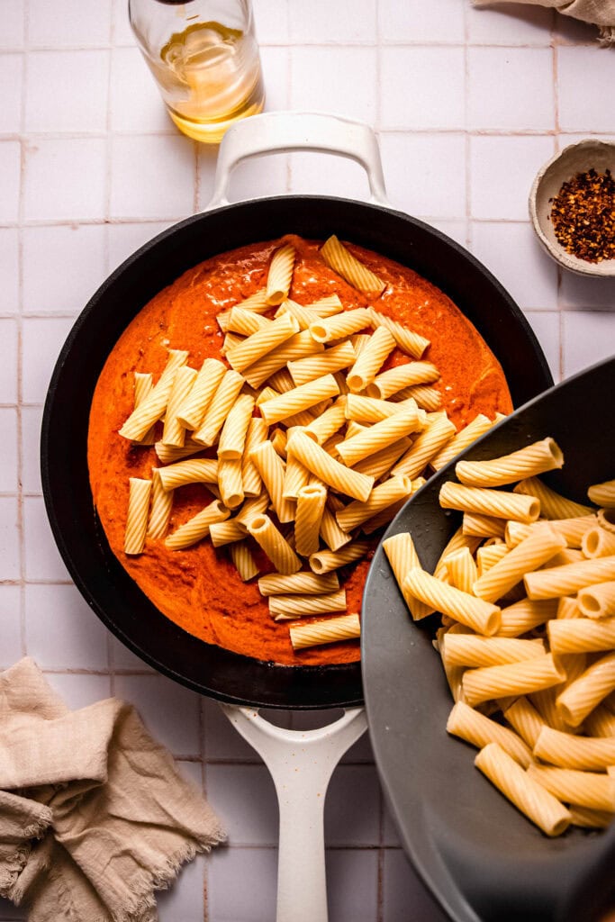 Cooked pasta being added to sauce.
