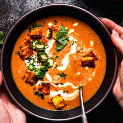 Hands holding bowl of butter chicken soup.