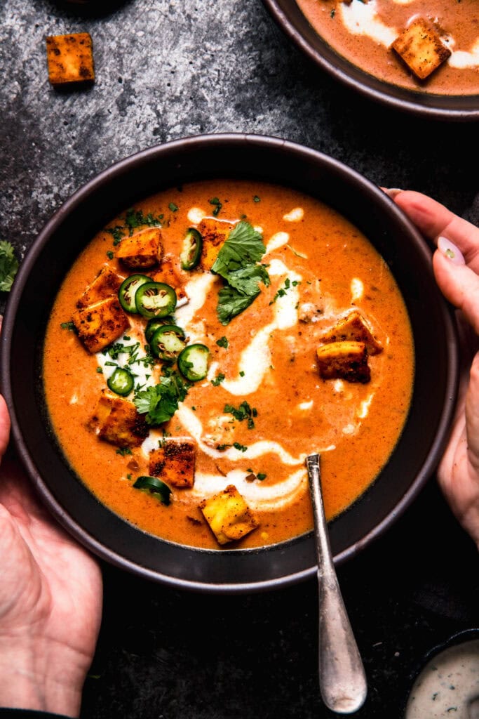 Hands holding bowl of butter chicken soup.