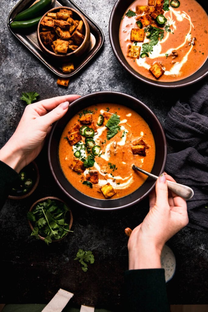 Hands holding bowl of butter chicken soup.