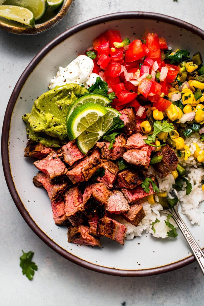 Overhead close up of Finished copycat chipotle steak bowl topped with corn salsa, guacamole and sour cream.