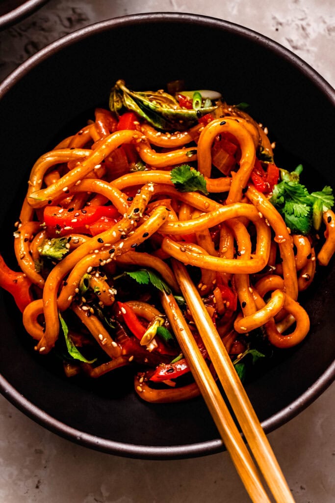 Black bowl of saucy gochujang noodles with chopsticks in an overhead view.